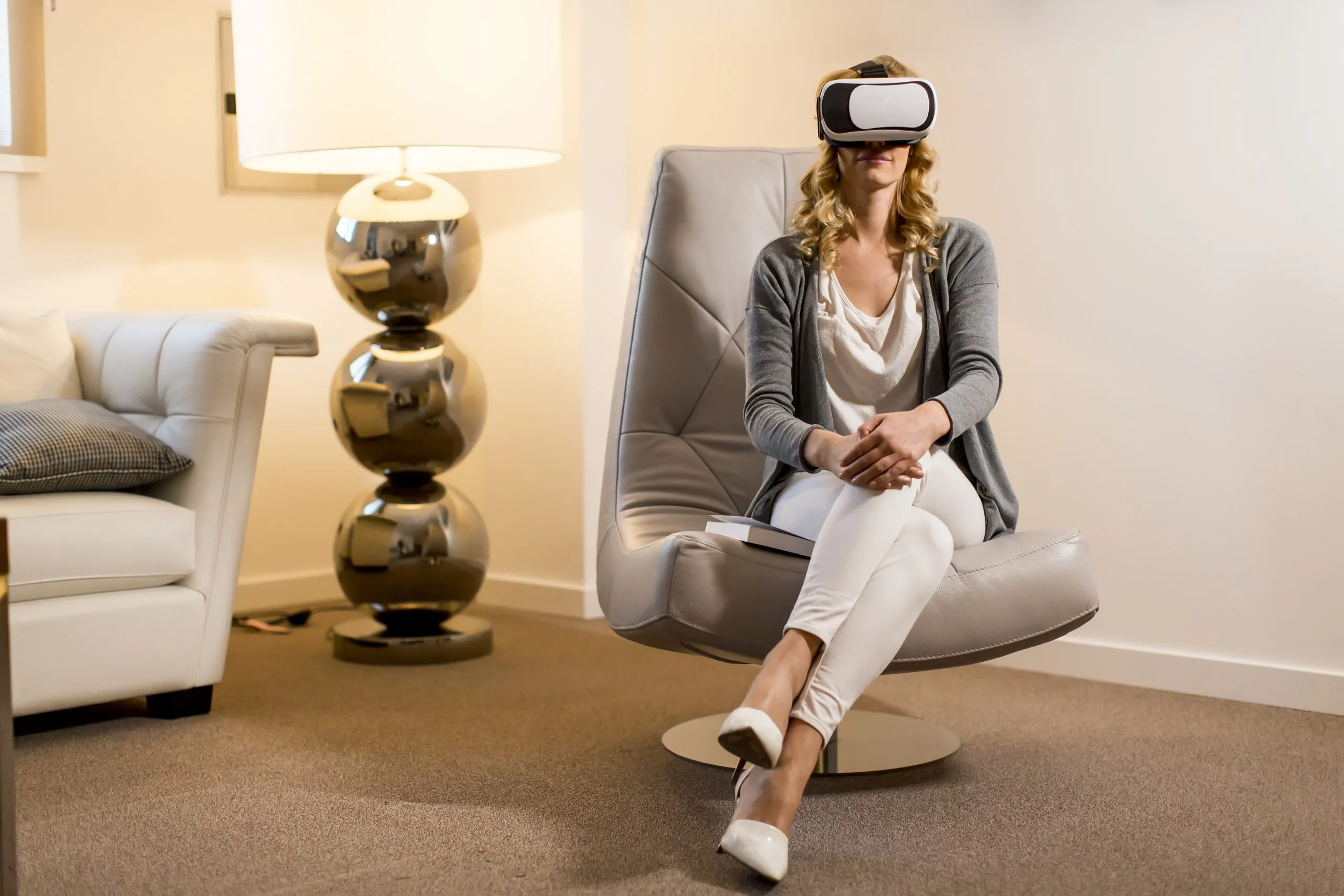 Femme assise dans un fauteuil confortable, un casque de réalité virtuelle sur les yeux, dans une pièce lumineuse